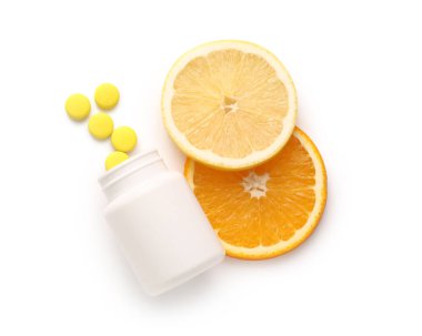 C vitamini hapları ve beyaz arka planda narenciye dilimleri olan bir şişe.