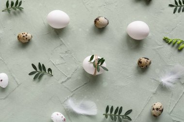 Yeşil arka planda yaprakları ve tüyleri olan Paskalya yumurtaları.