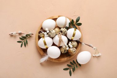 Wooden plate with Easter eggs, leaves, gypsophila flowers and pussy willow branches on beige background