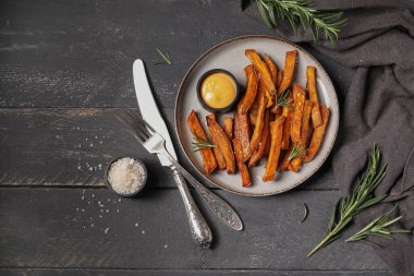 Lezzetli pişmiş patates tabağı ve siyah ahşap arka planda sos.