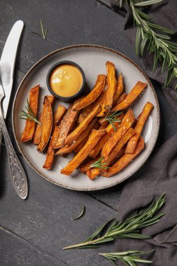 Lezzetli pişmiş patates tabağı ve siyah ahşap arka planda sos.