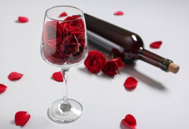 Beyaz arka planda kırmızı gül çiçekleri olan bir şişe şarap ve cam, yakın plan. Sevgililer Günü kutlaması