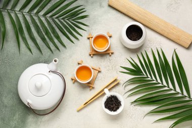 Çaydanlıklı kompozisyon, bir fincan siyah çay, kuru yapraklar ve yeşil grunge arka planda tropikal yapraklar.