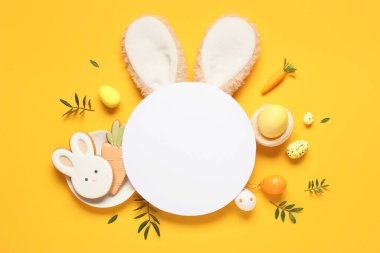 Sarı arka planda paskalya yumurtaları, kurabiyeler ve yeşil yapraklı kompozisyon