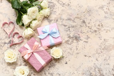 Bej rengi grunge arka planda hediye kutuları, kağıt kalpler ve beyaz gül çiçekleri olan kompozisyon