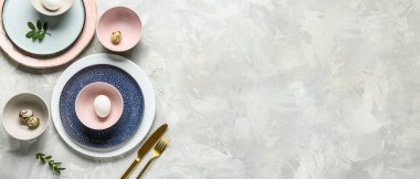 Farklı temiz tabaklar, paskalya yumurtaları ve gri arka planda yeşil yapraklar.