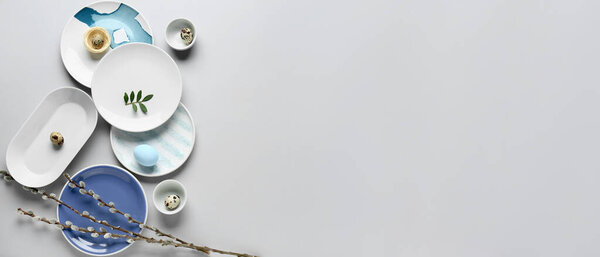 Different clean plates, Easter eggs and pussy willow branches on grey background with space for text