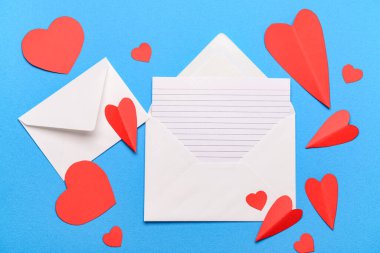 Boş kartlı zarflar ve mavi arka planda kırmızı kağıt kalpler. Sevgililer Günü kutlaması