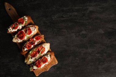 Siyah arka planda ricotta soslu lezzetli domates bruschetta tahtası.