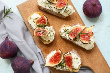 Lezzetli incir bruschetta tahtası ricotta peyniri ve açık mavi arka planda biberiye.