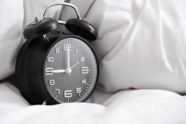 Yatağın üzerinde battaniyeli siyah çalar saat, yakın plan.