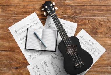 Ahşap zemin üzerinde Ukulele, defter, kalem ve nota kağıtları