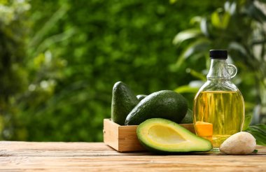 Dışarıdaki ahşap masada bir şişe taze yağ ve avokado.