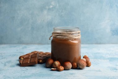 Kavanoz dolusu çikolata ve açık mavi arka planda fındık.