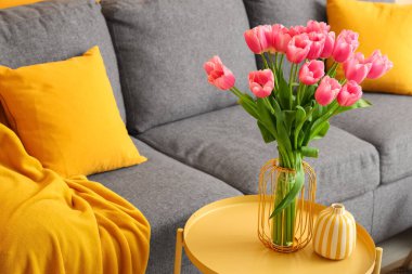 İçinde güzel lale çiçekleri olan bir vazo ve oturma odasındaki sehpanın üzerinde kitaplar, yakın plan.