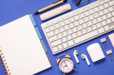 Alarmlı klavye, kulaklık ve mavi arka planda ofis kırtasiyesi.