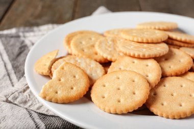 Kahverengi ahşap arka planda lezzetli krakerler olan tabak, yakın plan.