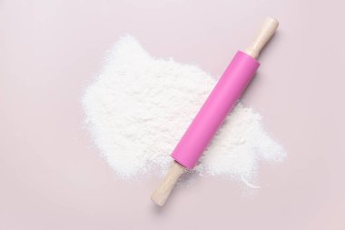 Açık pembe arka planda yuvarlanan iğne ve un