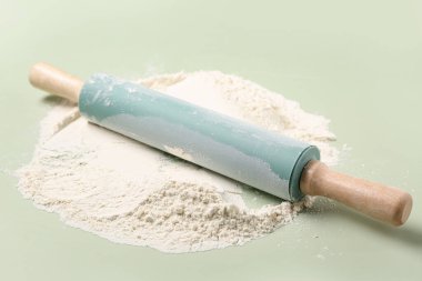 Açık yeşil arkaplanda yuvarlanan iğne ve un, yakın plan.