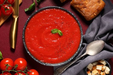 Bir kase lezzetli domates çorbası ve kırmızı grunge arka planda malzemeler, yakın plan.