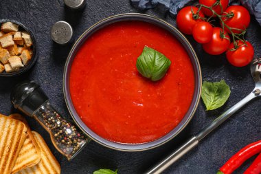 Bir kase lezzetli domates çorbası ve siyah grunge arka planda malzemeler, yakın plan.