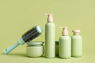 Saç spreyi şişeleri, kozmetik ürünler kavanozu ve yeşil arka planda fırça.