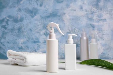 Mavi grunge duvarının yanındaki beyaz masada saç spreyi şişeleri