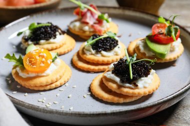 Peynirli, domatesli ve siyah havyarlı farklı lezzetli krakerler. Gri ahşap arka planda, yakın planda.