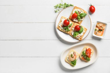 Peynirli, domatesli, somonlu ve karidesli leziz krakerler beyaz ahşap arka planda.