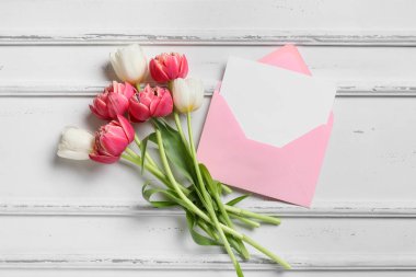 Güzel bir buket lale çiçeği ve beyaz ahşap arka planda bir zarf.