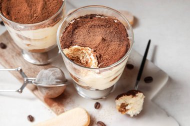 Tatlı tiramisulu bardaklar, beyaz arka planda kurabiye ve kahve çekirdekleri.