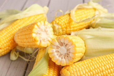 Gri ahşap arka planda taze mısır koçanları, yakın plan.