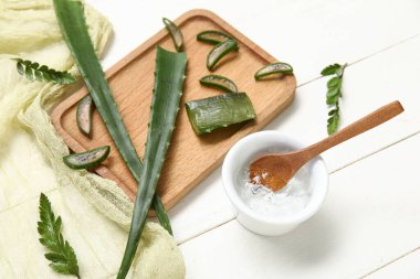 Beyaz ahşap arka planda yaprakları olan bir kase aloe vera jel ve tahta.
