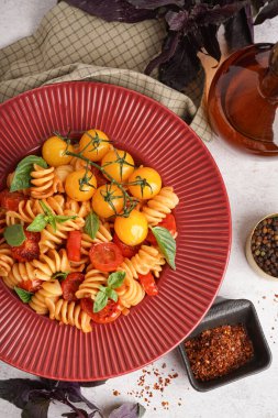 Beyaz arka planda domatesli ve fesleğenli lezzetli fusilli makarna.
