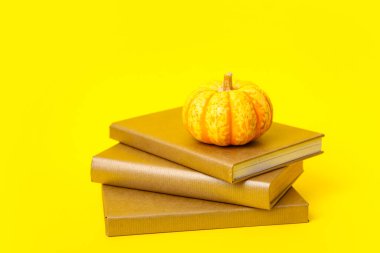 Kitap yığını ve sarı arka planda olgun balkabağı