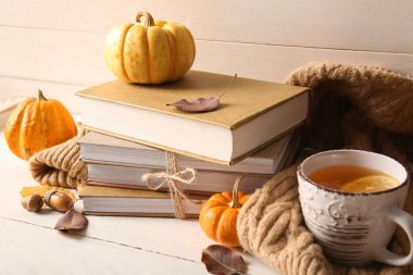 Kitap yığını, çay fincanı, sıcak süveter ve açık ahşap masadaki balkabakları.