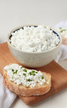 Taze süzme peynirli kase ve beyaz ahşap arka planda ekmek dilimleri.