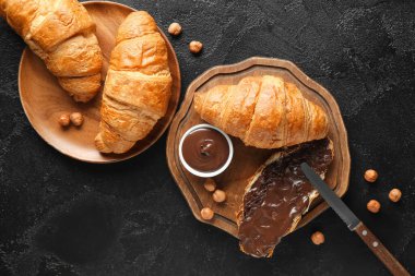 Çikolata kaplı tatlı kruvasanlar ve siyah arka planda fındıklar.