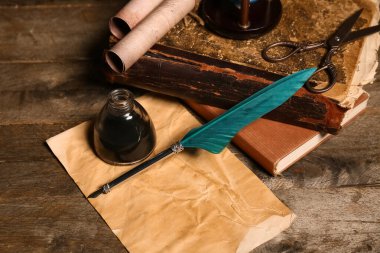 Ahşap zemin üzerinde kalem, mürekkep, parşömen ve makas olan eski kitaplar