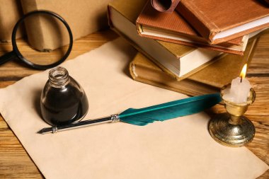 Ağaç zemin üzerinde kalem, mürekkep hokkası, büyüteç ve mum olan kitaplar.