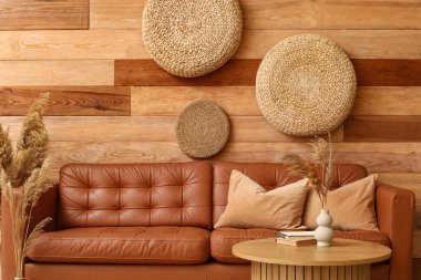 Yumuşak yastıklı kahverengi deri kanepe ve oturma odasındaki tahta duvarın yanındaki masa.