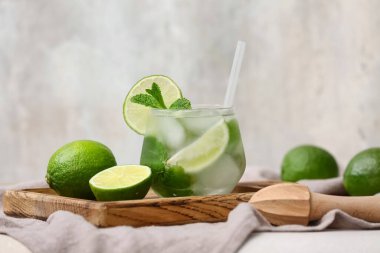 Ahşap tepsi, bir bardak lezzetli mojito, gri arka planda peçete ve malzemeler, yakın plan.