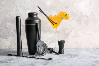 Gri grunge arka planında bir bardak kokteyl olan farklı barmen aletleri.