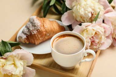 Tatlı kruvasanla güzel şakayık çiçekleri ve bej arka planda bir fincan kahve.