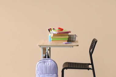 Sırt çantası, kitaplar ve bej arka planı olan modern okul masası.