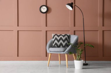 Yumuşak yastıklı rahat gri koltuk ve oturma odasındaki kahverengi duvarın yanındaki lamba.