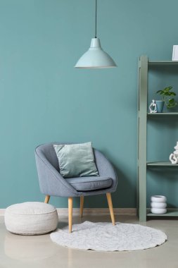 Oturma odasındaki nane duvarının yanında rahat koltuk, puf ve raf ünitesi, yakın plan.