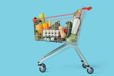 Mavi arka planda farklı taze ürünleri olan alışveriş arabası.