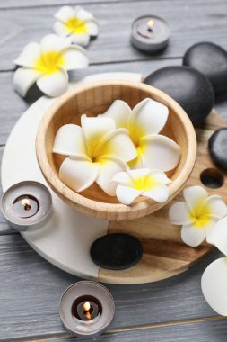 Gri ahşap arka planda tepsi, taş ve su tesisatı çiçekli güzel bir spa kompozisyonu, yakın plan.