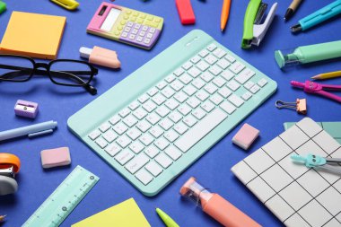 Modern bilgisayar klavyesi, gözlük ve mavi zemin üzerinde farklı kırtasiye malzemesi olan kompozisyon